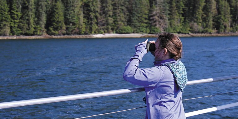 Ein junges Mädchen schaut an Deck eines Kreuzfahrtschiffes durch ein Fernglas