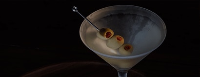 A classic dirty martini is served in a frosted cocktail glass against a dark, dramatic background